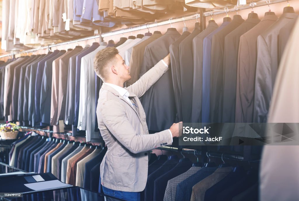 cheerful male customer examining suits in men’s cloths store